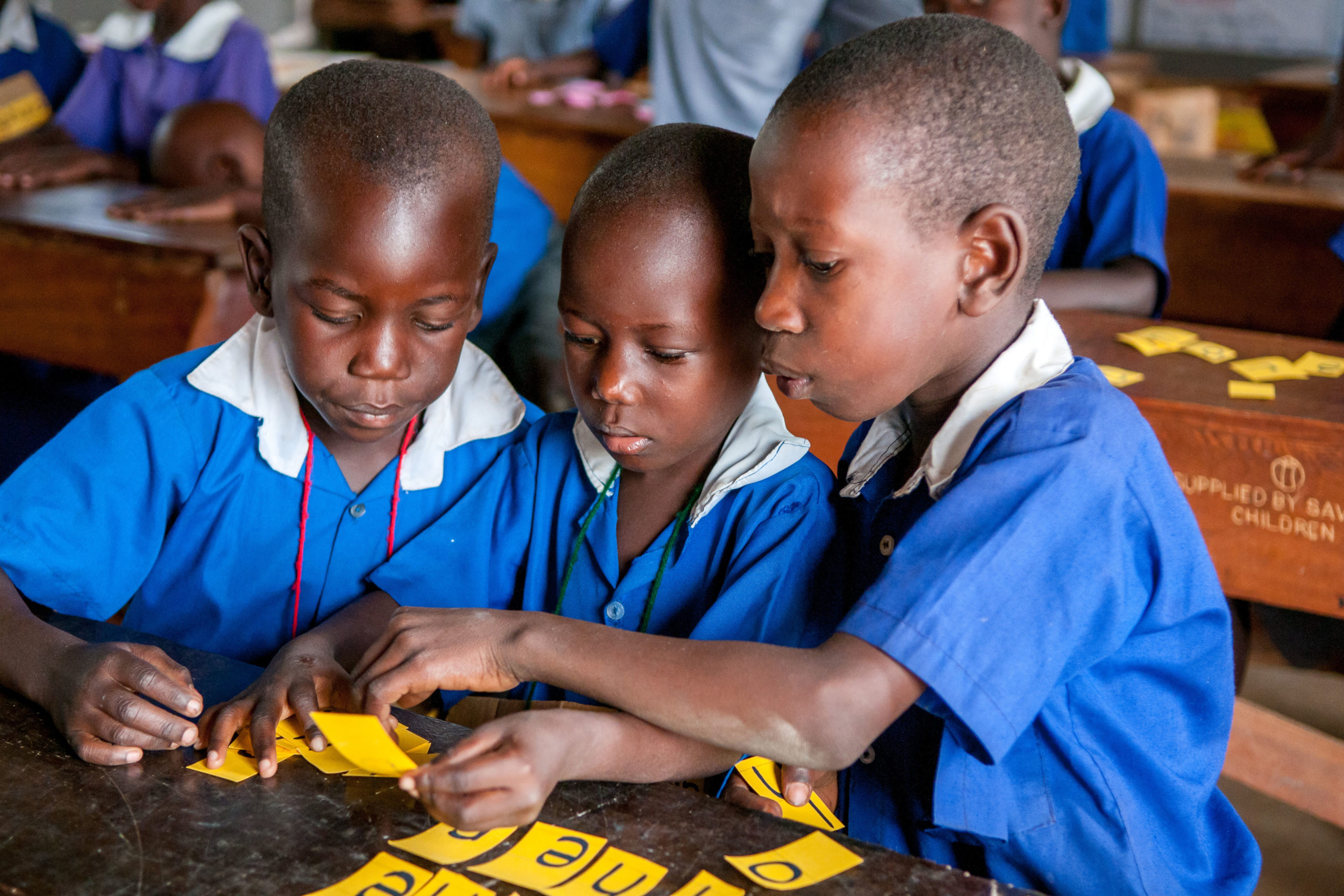 Tre børn med bogstaver i skoleklasse, Uganda
