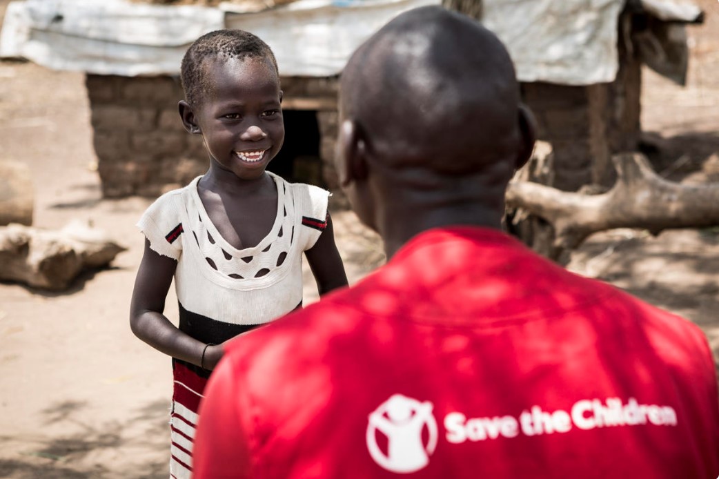 En lille pige smiler stort til en Red Barnet medarbjeder
