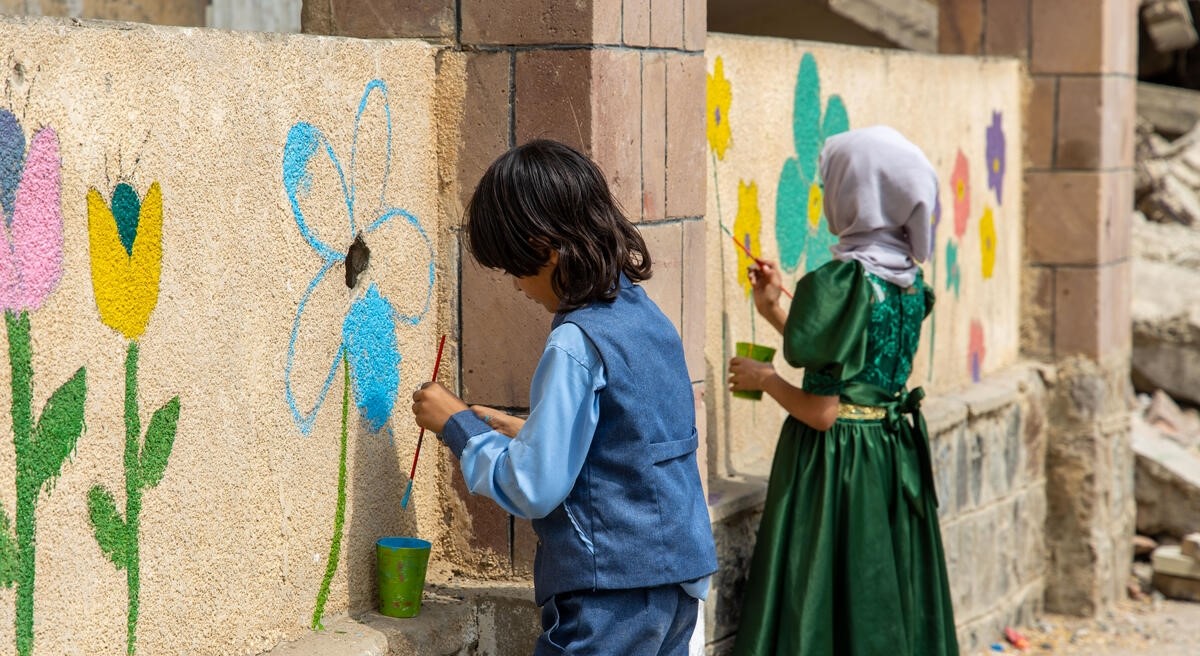 Børn i Yemen maler farverige blomster på ruiner i byen