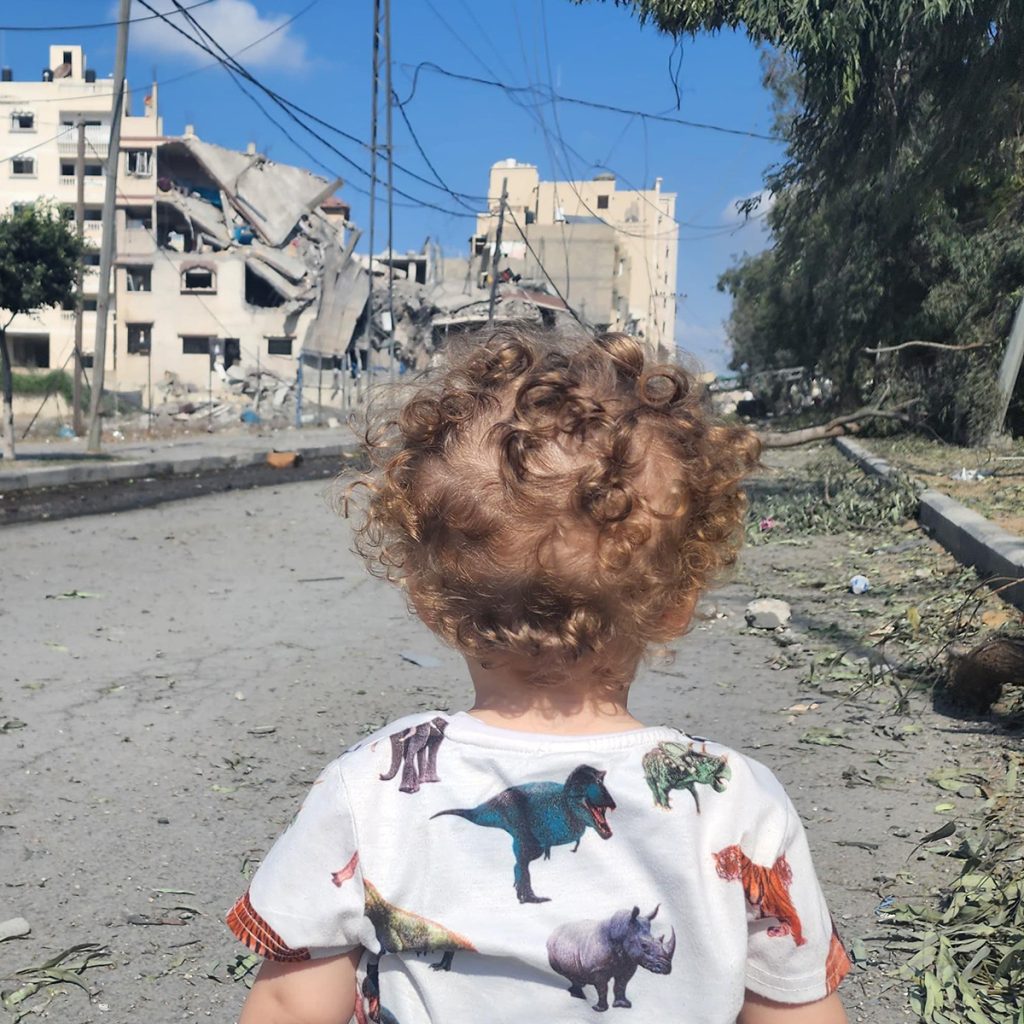 2-årog dreng, Gaza med ødelagt bygning i baggrunden