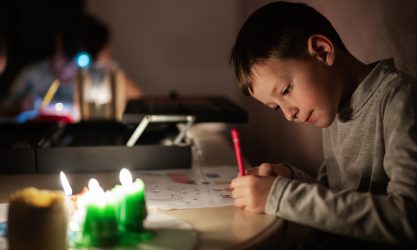 Barn sidder og tegner ved bord med stearinlys