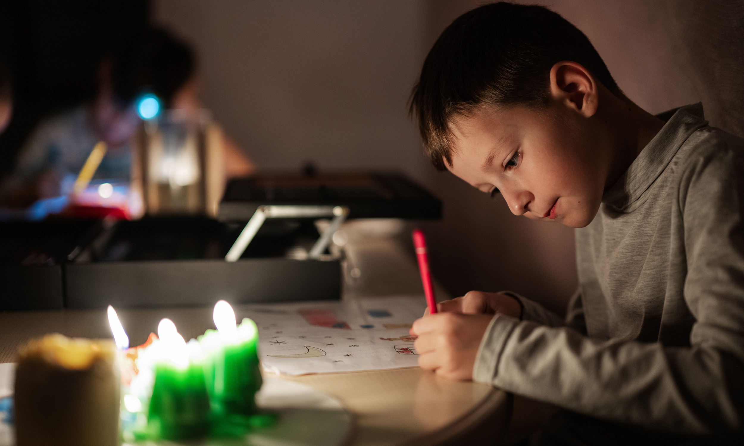 Barn sidder og tegner ved bord med stearinlys