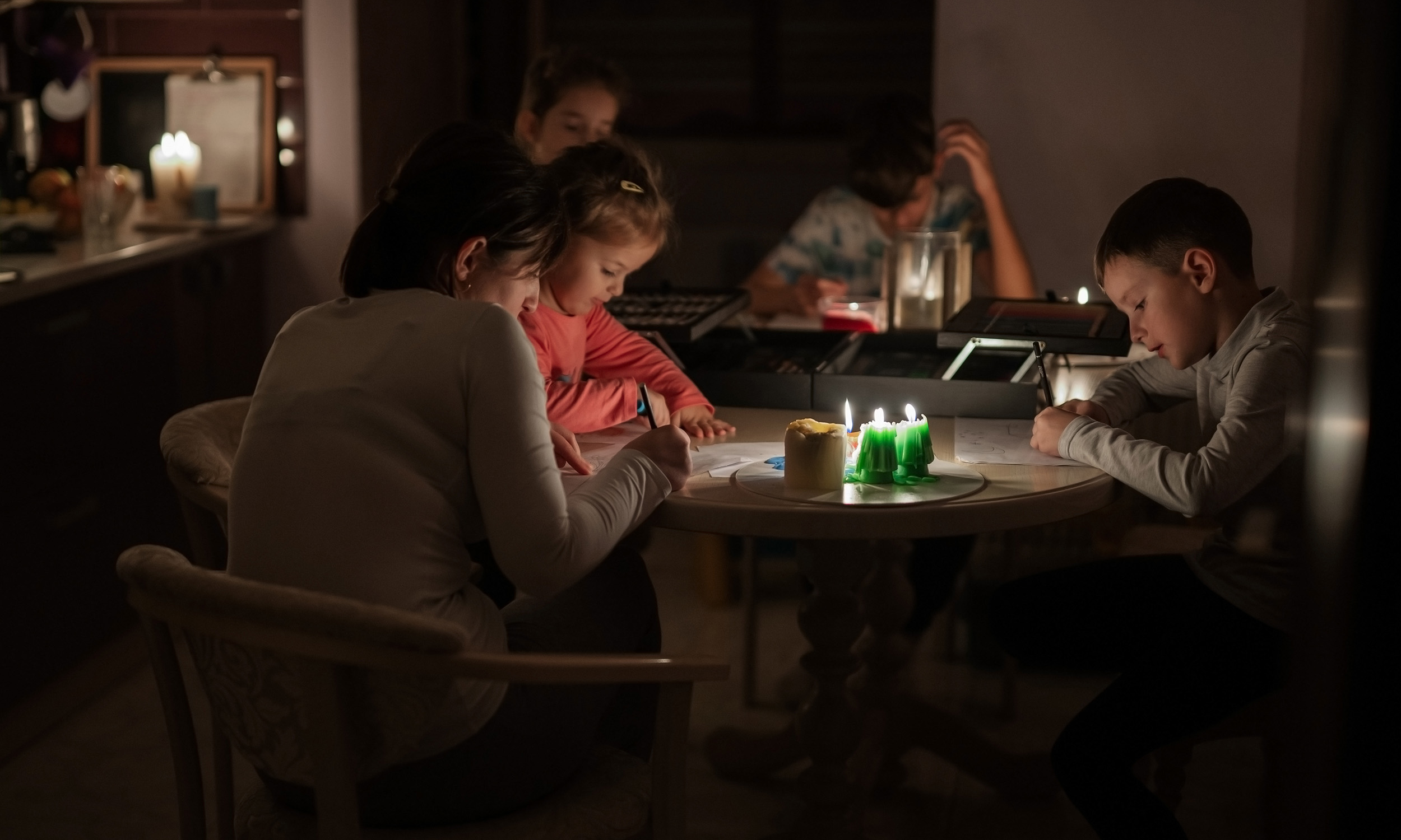 Voksne og børn sidder ved bord med stearinlys